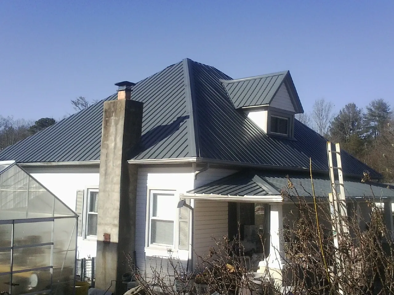 Dark blue standing seam metal roof on a white farmhouse with dormer — Slate & Tile Roof Repair by Roofing Brothers in Haywood