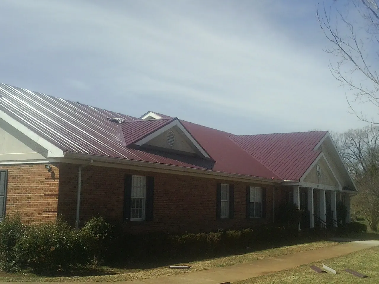 Red metal roof with gabled entries on a long brick building, from a Hail Damage Roof Repair job in Haywood