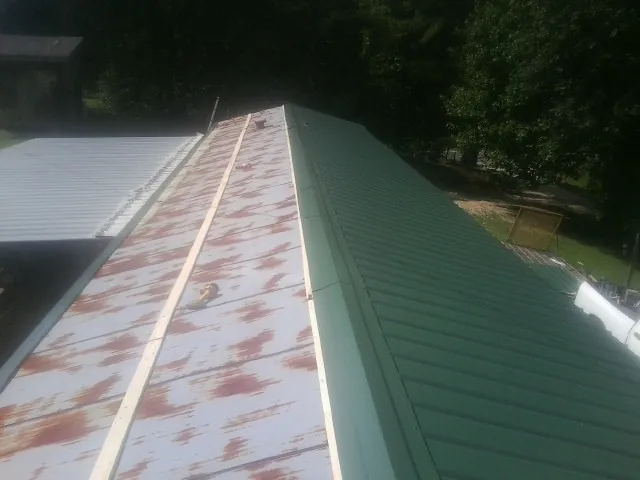 Old rusted panels beside newly installed green metal roofing — Wind Damage Roof Repair by Roofing Brothers in Haywood