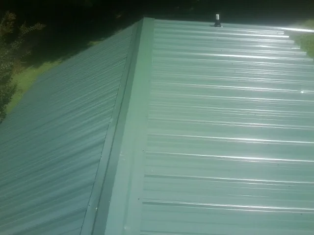 New green metal panels meeting at the ridge of a roof — Flat Roof Repair work by our crew in Haywood