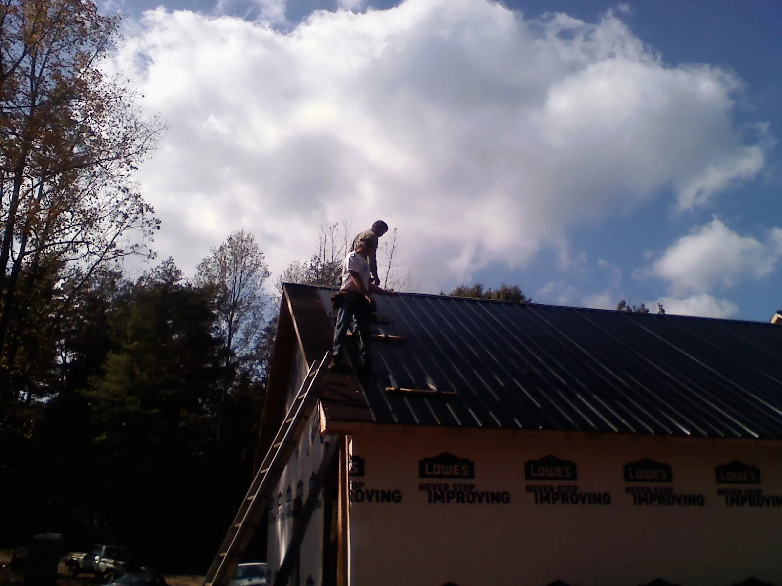 Roofer fastening dark metal panels high against a cloudy sky, from a Roof Inspection job in Haywood