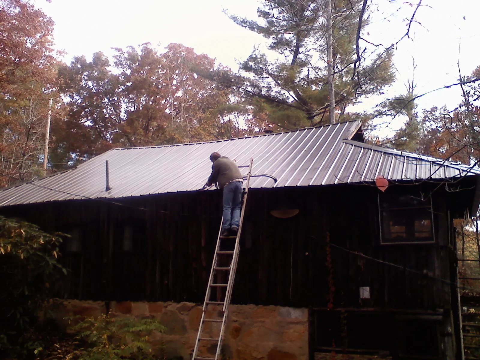 Roofer on a ladder working along the edge of a cabin metal roof in Haywood