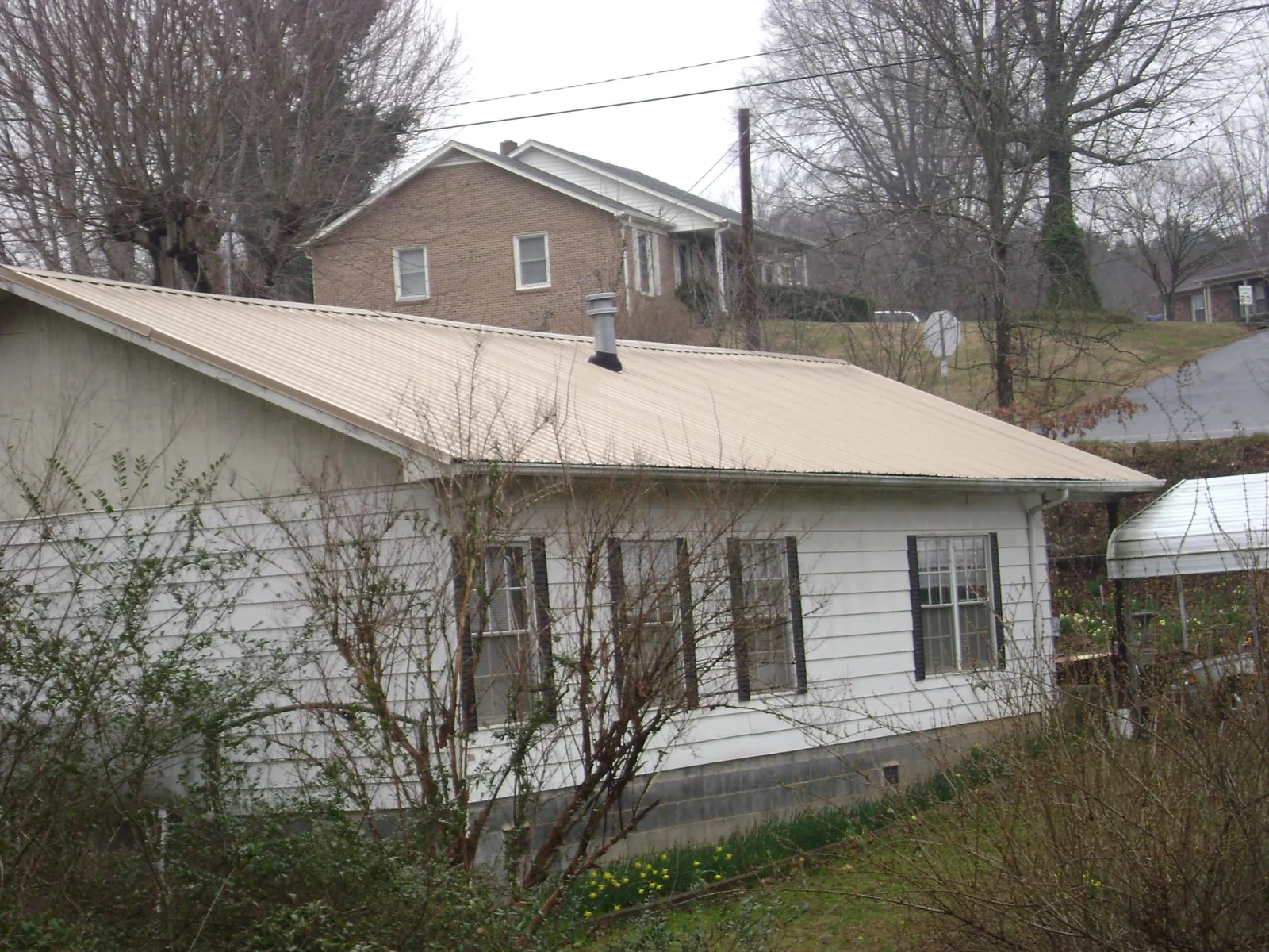 Tan metal roof on a white sided house set into a hillside — Commercial Roofing by Roofing Brothers in Haywood
