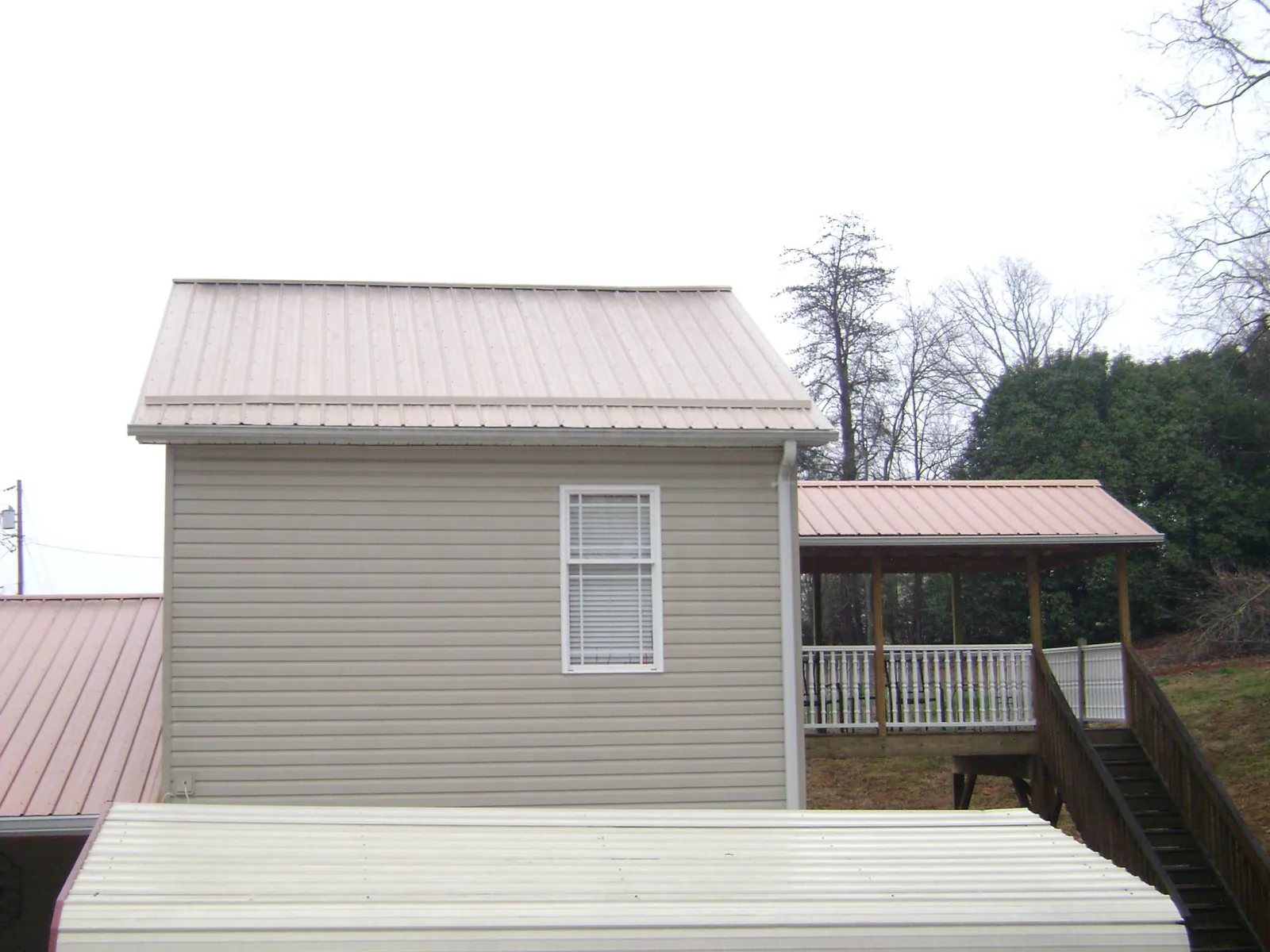 Tan metal roofs on a two story addition and attached porch, from a Roof Replacement job in Haywood